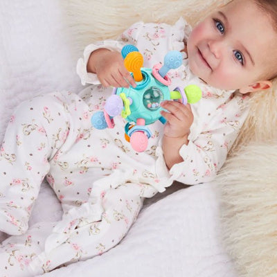 Hochet-bebe-turquoise-dans les mains d'un bébé couché dans son lit