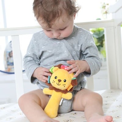 Hochet bébé musical lion jaune dans la main d'un bébé habillé en gris et assis dans son lit