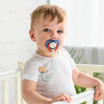 Attache-tétine-bleu-coeur-bois bébé assis dans son lit