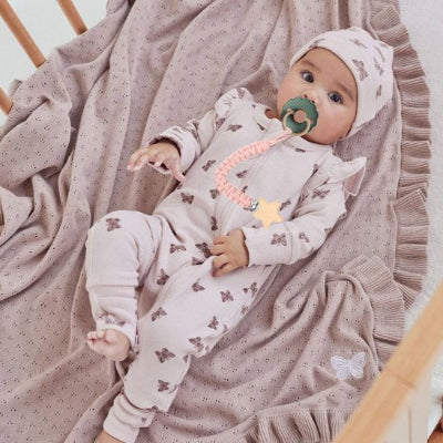 Attache-tétine-rose-étoile-bois bébé couché habillé avec un tenu beige motif papillon