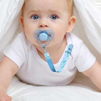 Attache tétine en silicone bleu dans la bouche d'un bébé et attaché à son Tshirt blanc