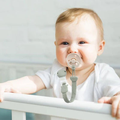 Attache tétine motif girafe vert dans la bouche bébé souriant debout dans son lit