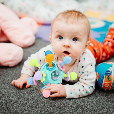 Hochet-bebe-turquoise-dans les mains d'un bébé couché sur le ventre