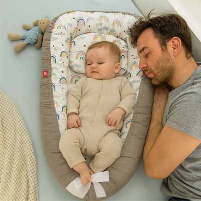 Réducteur de lit arc en ciel bébé endormi paisiblement à côté de papa