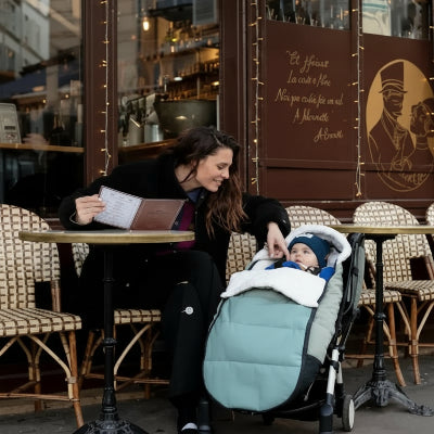 chancelière poussette aqua dans un café maman  habillée en noir carasse la joue de son bébé