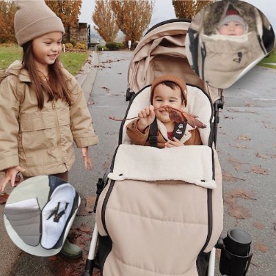 Chancelière-poussette-taupe-fillette-souriante-dans-la-rue-avec-bébé-tient-une-feuille-d'arbre-dans-chancelière-poussette