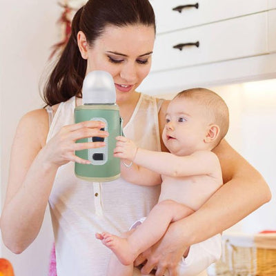 chauffe biberon attachable vert dans la main de maman et porte bébé dans l'Autre bras