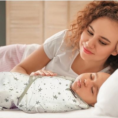 Couverture-d'emmaillotage-motif-étoiles-enveloppant-bébé-endormi-maman-le-regardant-souriante