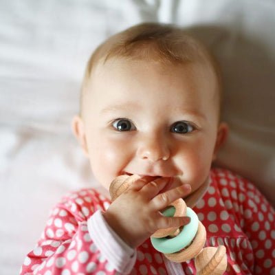 Hochet bebe en silicone vert dans la bouche d'un bébé souriant