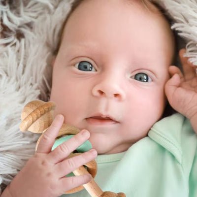 Hochet bebe en bois vert dans les mains d'un bébé avec yeux verts